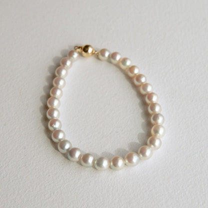 A single-strand pearl bracelet with a gold clasp and Broken Bay grown Australian Akoya pearls, displayed on a textured off-white surface.