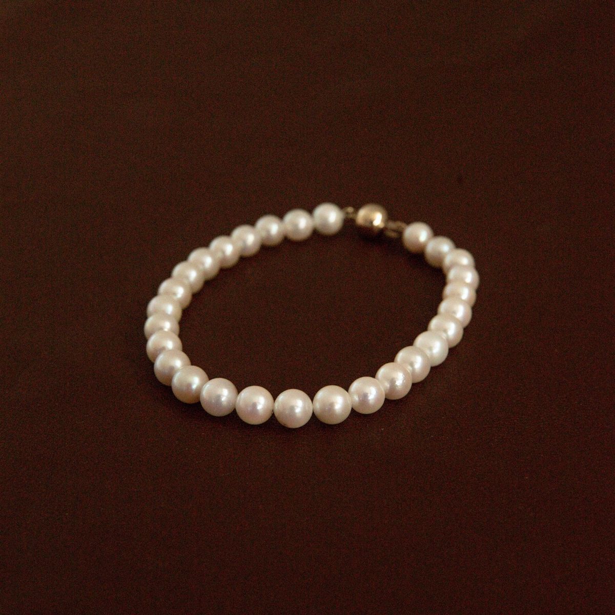 A string of Australian Akoya pearls set on a pearl bracelet with a gold clasp, displayed on a dark brown background.