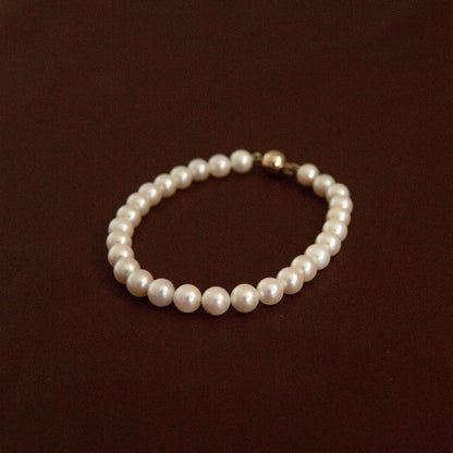 A string of Australian Akoya pearls set on a pearl bracelet with a gold clasp, displayed on a dark brown background.