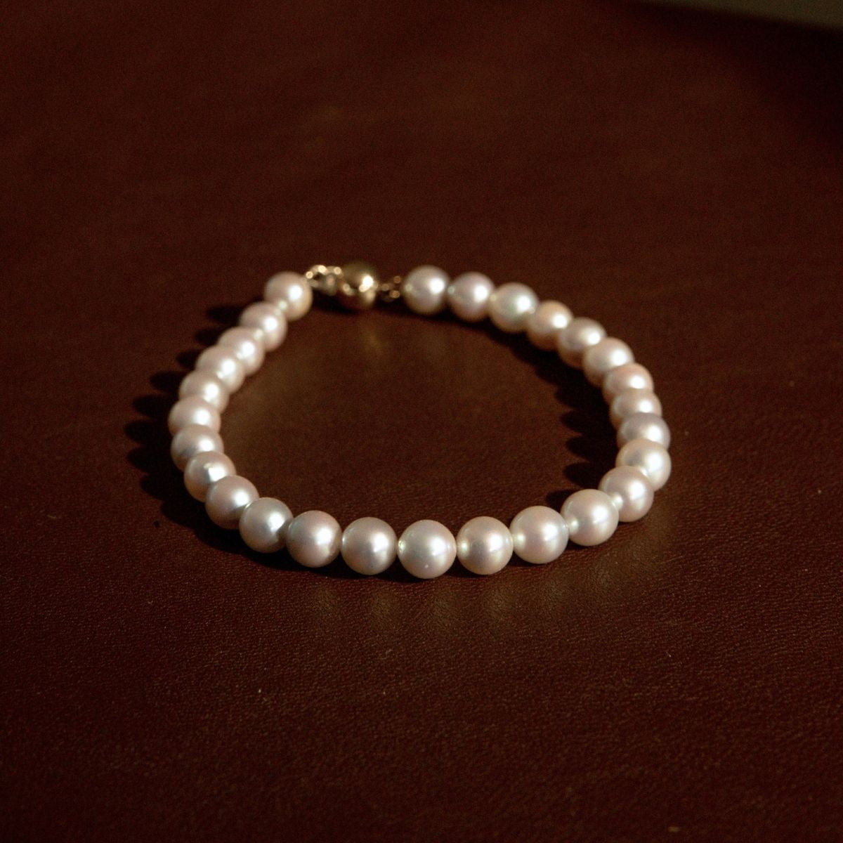 A classic pearl strand bracelet with a gold clasp, resting on a dark brown surface.
