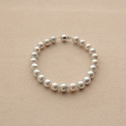 A strand bracelet made of round white Broken Bay grown Akoya pearls with a 9ct white gold ball clasp, displayed on a textured beige surface.
