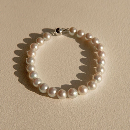 A single-strand pearl bracelet with a 9ct white gold ball clasp, displayed on a textured beige surface with a soft shadow.