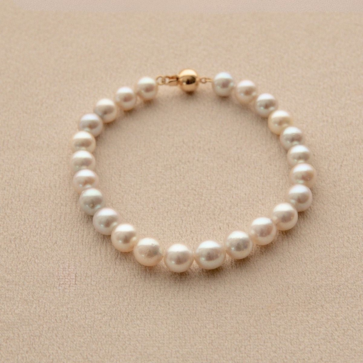 An Australian Akoya pearl bracelet with an 18ct yellow gold clasp, displayed on a textured beige surface.