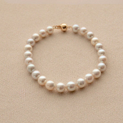 An Australian Akoya pearl bracelet with an 18ct yellow gold clasp, displayed on a textured beige surface.