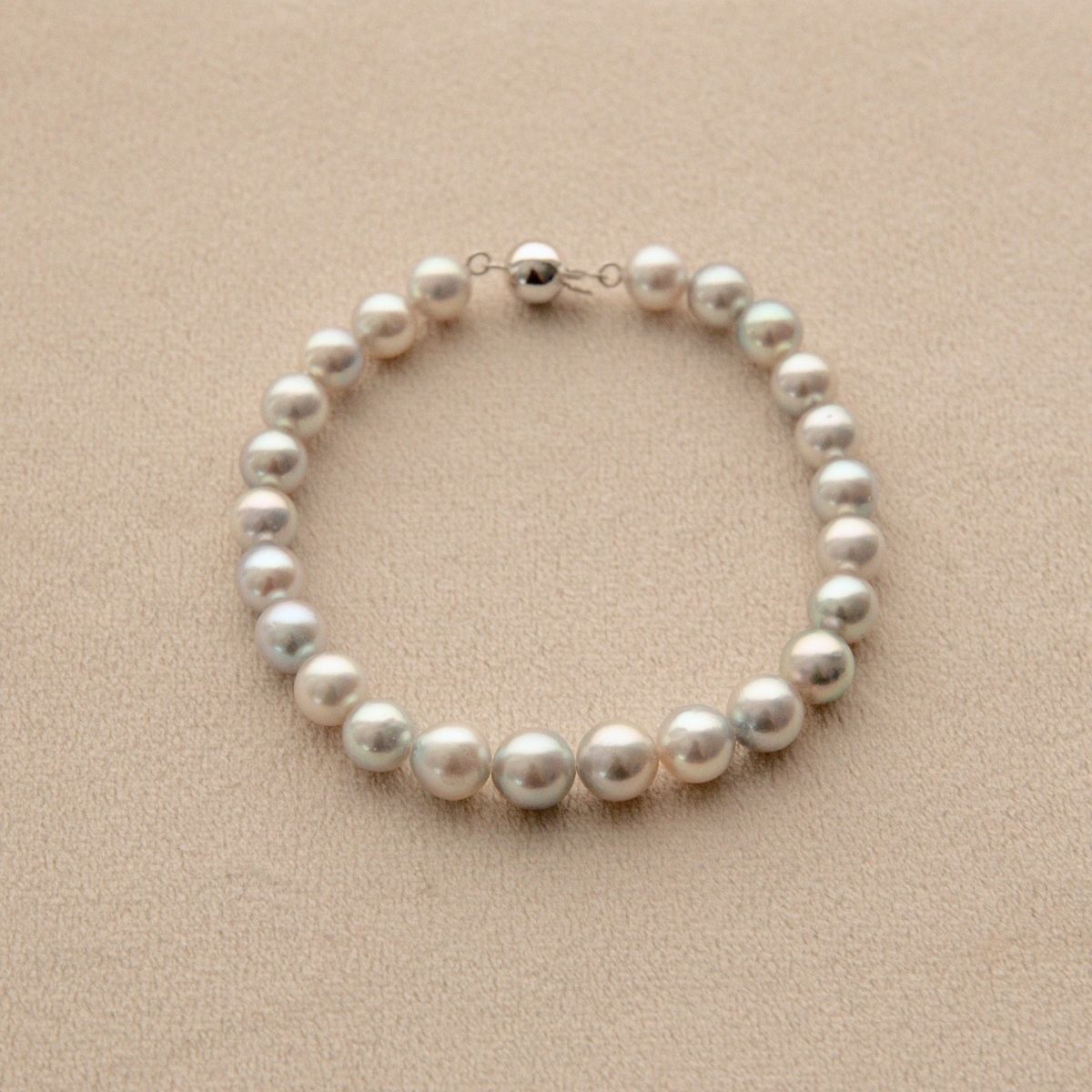 A single-strand pearl bracelet with a 18ct white gold ball clasp, displayed on a textured beige surface.