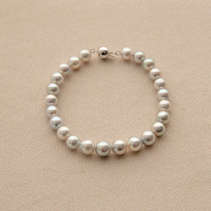 A single-strand pearl bracelet with a 18ct white gold ball clasp, displayed on a textured beige surface.