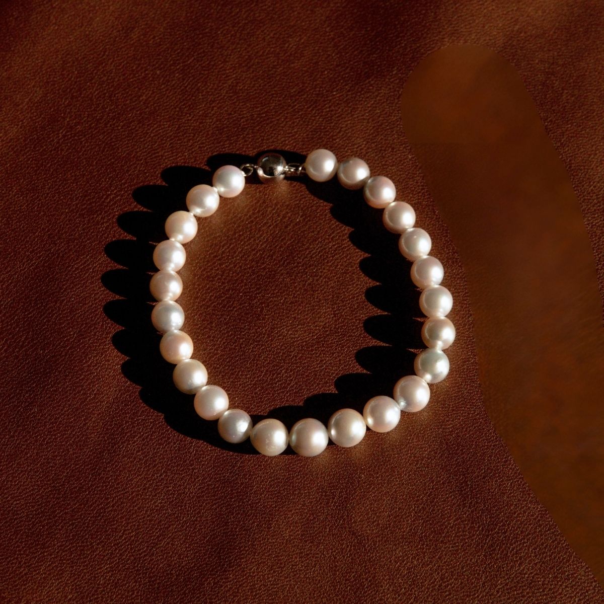 A classic pearl strand bracelet with an 18ct ball clasp, arranged in a circle on a textured brown leather background.