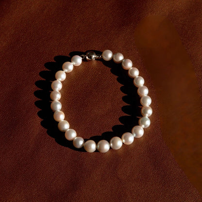 A classic pearl strand bracelet with an 18ct ball clasp, arranged in a circle on a textured brown leather background.