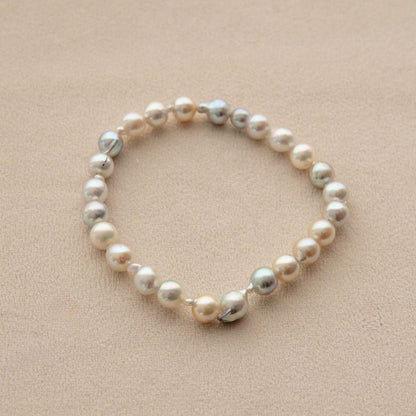 An Akoya pearl bracelet made of mixed Saltwater pearls in white, cream, and iridescent silver tones, displayed on a textured beige background.