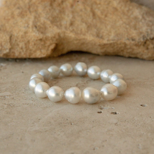A pearl strand bracelet made of baroque Australian South Sea pearls, displayed on a textured beige stone surface with a larger tan rock in the background.