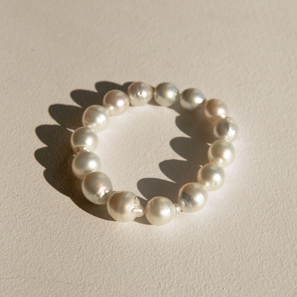 A stretchy pearl strand bracelet made of irregular Cygnet Bay grown Australian South Sea pearls, arranged in a circle on a textured beige surface with a soft shadow.