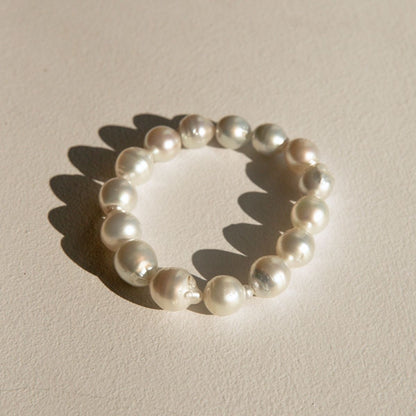 A stretchy pearl strand bracelet made of irregular Cygnet Bay grown Australian South Sea pearls, arranged in a circle on a textured beige surface with a soft shadow.