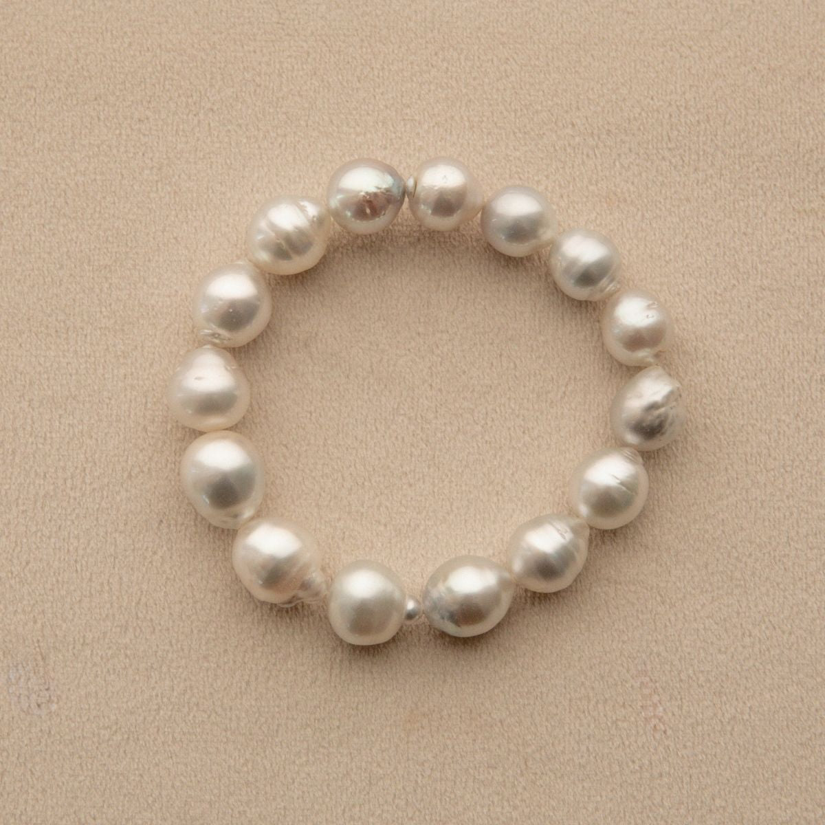 An Australian South Sea pearl strand bracelet made of irregular, lustrous white Cygnet Bay pearls, displayed on a textured beige surface.