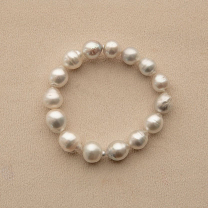 An Australian South Sea pearl strand bracelet made of irregular, lustrous white Cygnet Bay pearls, displayed on a textured beige surface.
