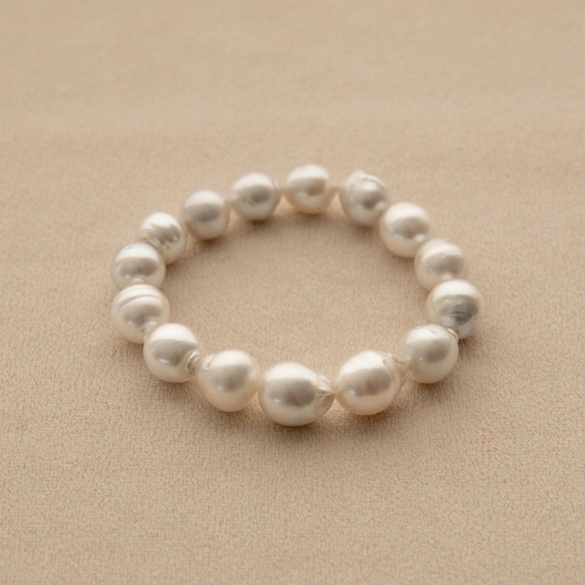 An elasticated pearl strand bracelet made of irregular Australian South Sea pearls, displayed on a textured beige surface.