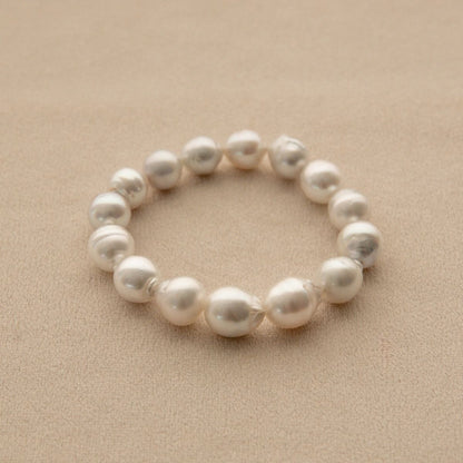 An elasticated pearl strand bracelet made of irregular Australian South Sea pearls, displayed on a textured beige surface.