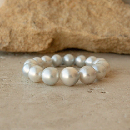 An elasticated pearl strand bracelet made of large, lustrous white Australian South pearls, displayed on a textured beige stone surface with a larger tan rock in the blurred background.