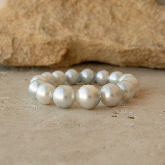 An elasticated pearl strand bracelet made of large, lustrous white Australian South pearls, displayed on a textured beige stone surface with a larger tan rock in the blurred background.