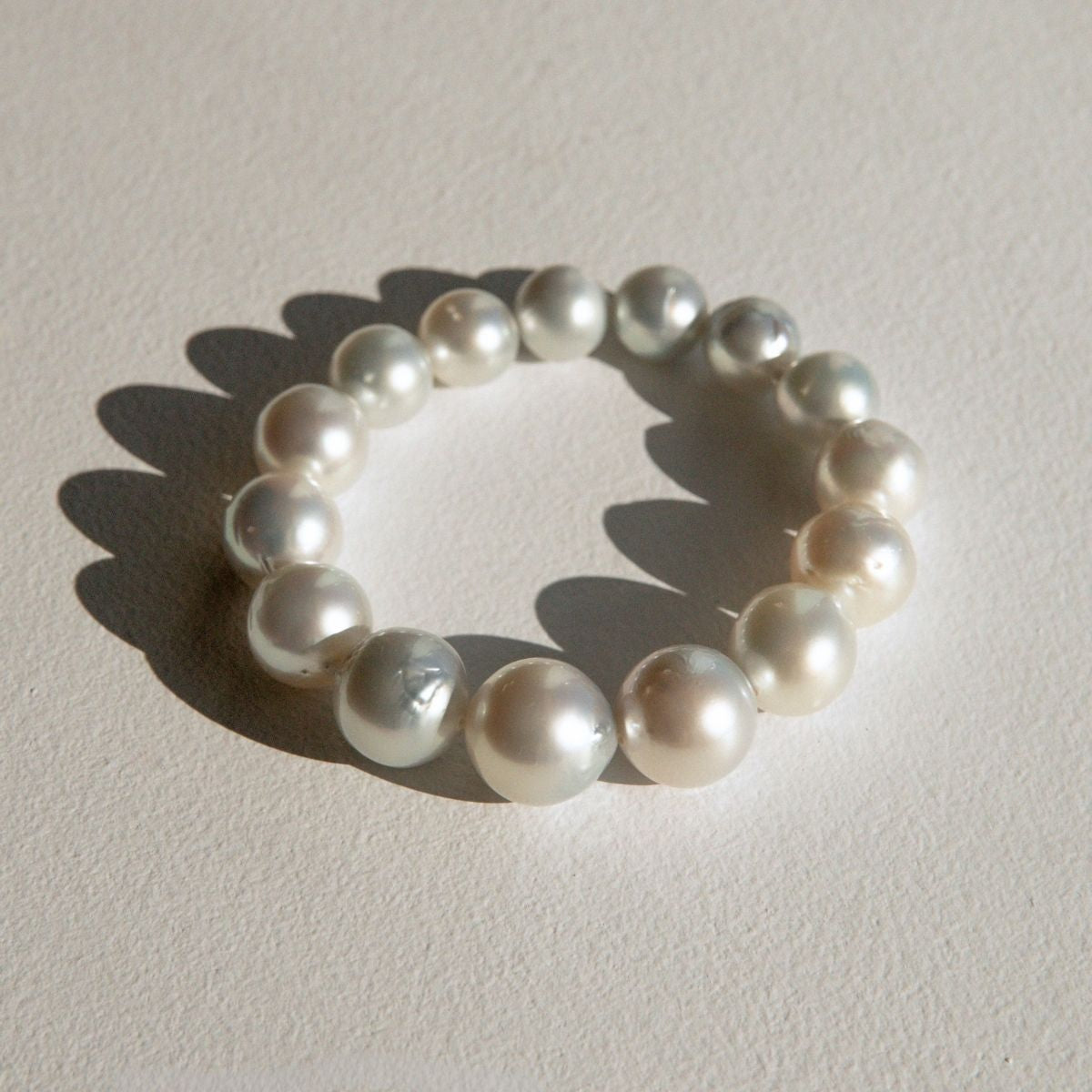 A pearl strand bracelet made of irregular Australian South Sea pearls, arranged in a circle on a textured off-white surface with a soft shadow.