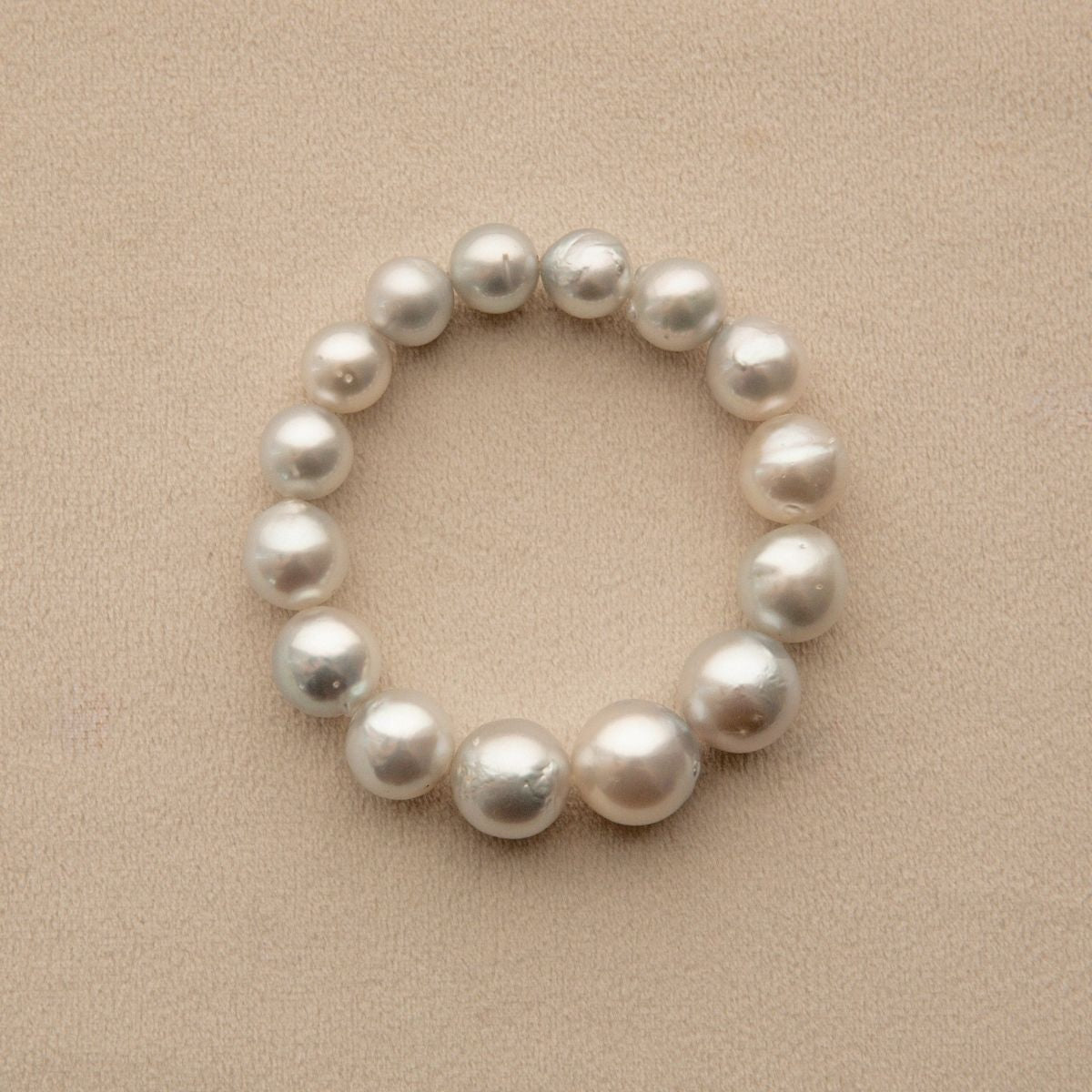 An elasticated pearl strand bracelet made of baroque shape Australian South Sea pearls, arranged in a circle on a textured beige background.