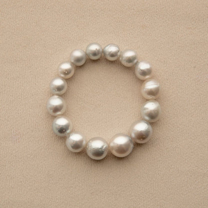An elasticated pearl strand bracelet made of baroque shape Australian South Sea pearls, arranged in a circle on a textured beige background.