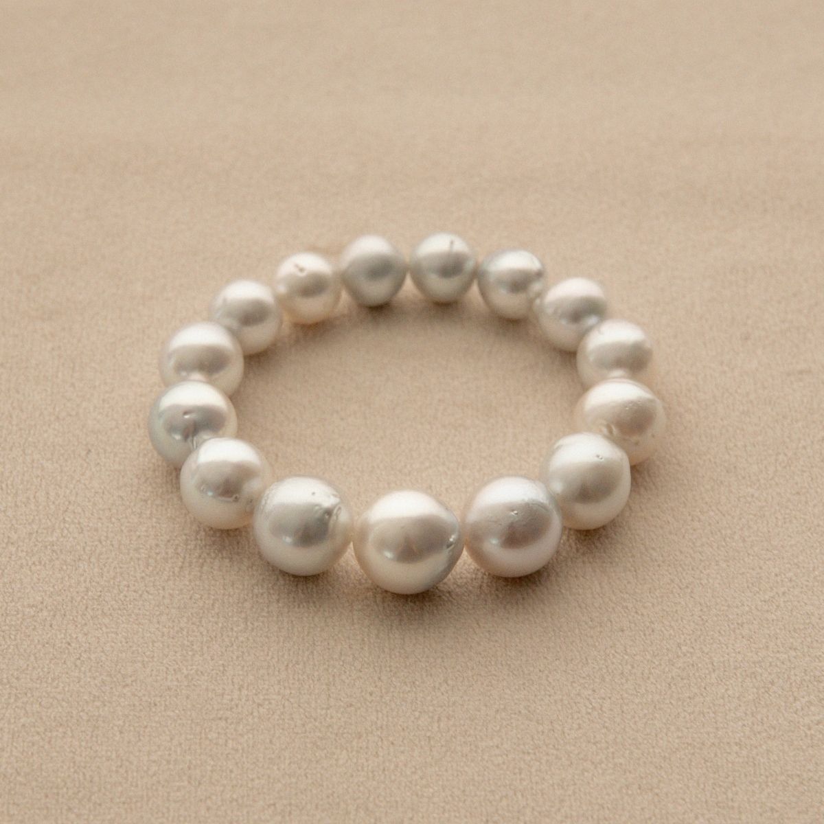 An Australian South Sea pearl strand bracelet made of baroque shape pearls, displayed on a textured beige background.