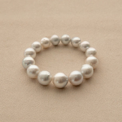 An Australian South Sea pearl strand bracelet made of baroque shape pearls, displayed on a textured beige background.