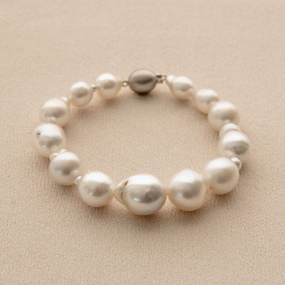 A strand bracelet made of irregular white South Sea pearls and a single 9ct white gold ball clasp, displayed on a textured beige background.