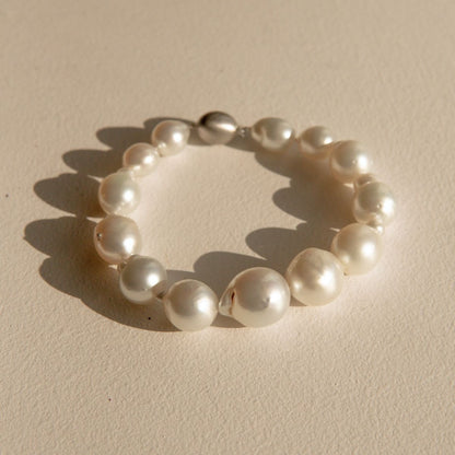 A baroque pearl bracelet with irregular white Australian South Sea pearls and a 9ct white gold clasp, photographed on a textured beige surface with a soft shadow.