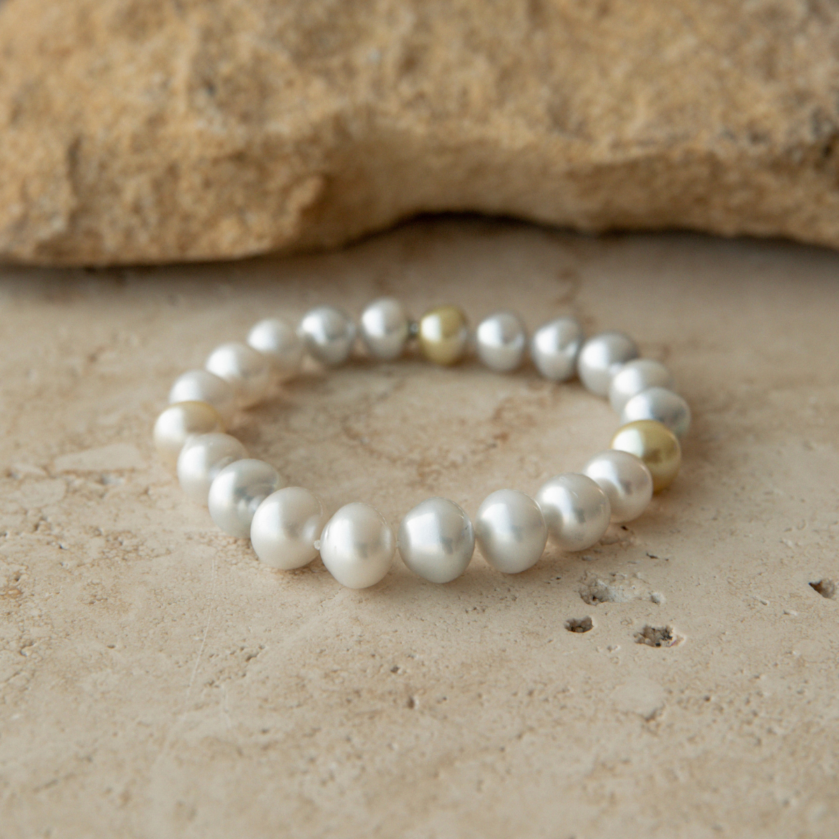 Pearl strand bracelet on a textured beige surface with a stone in the background
