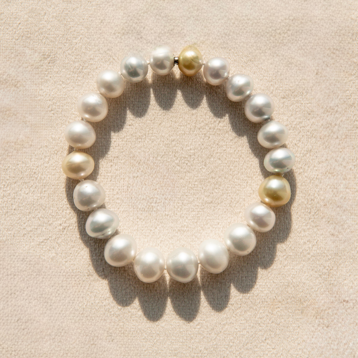 Pearl strand bracelet with gold accents on a beige fabric background