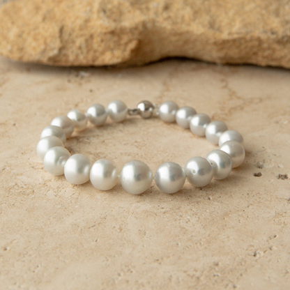 Pearl strand bracelet on a sandy surface with a rock in the background