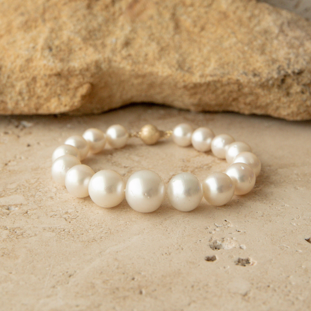 Graduated pearl strand bracelet on a textured beige surface with a rock in the background