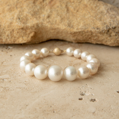 Graduated pearl strand bracelet on a textured beige surface with a rock in the background