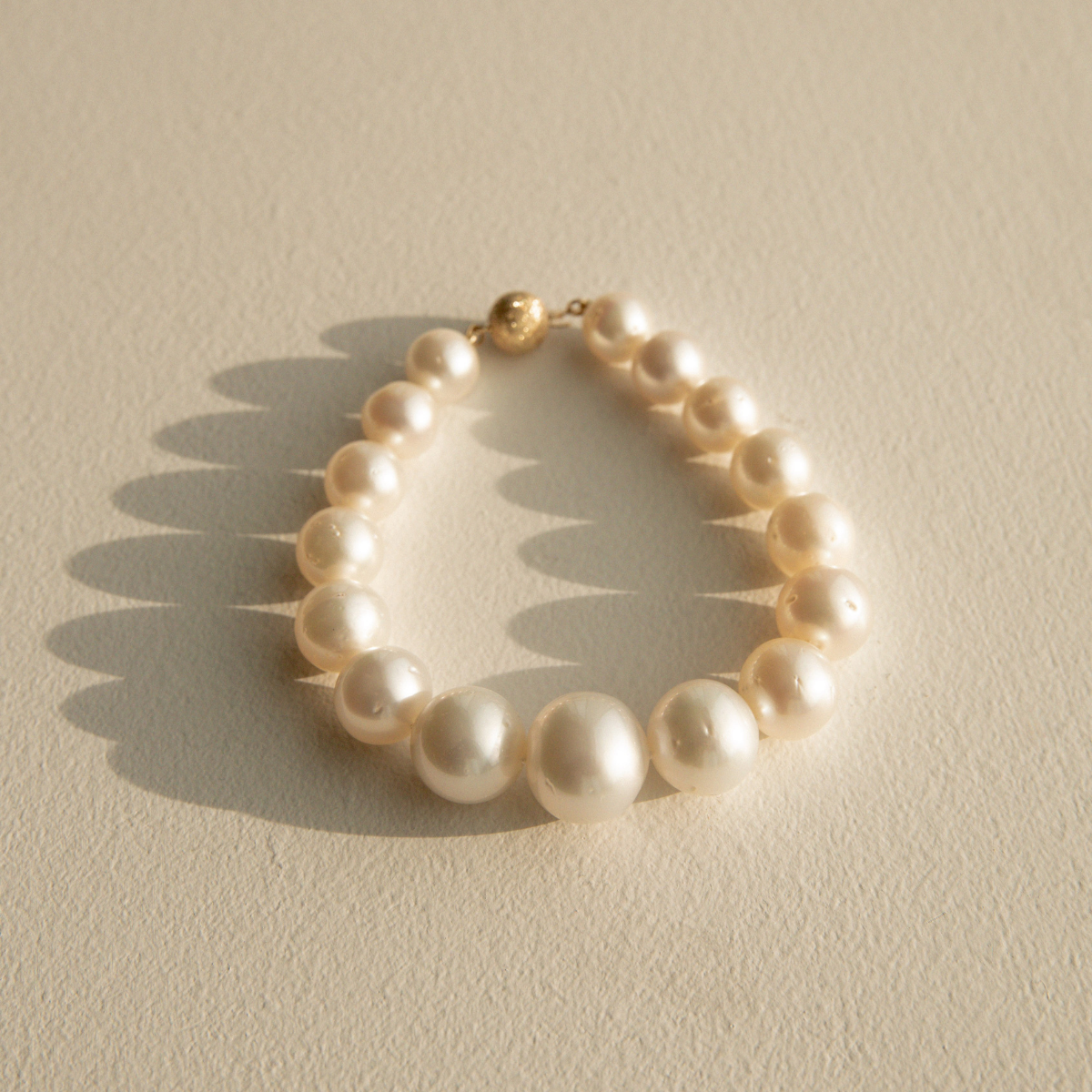 Graduated pearl strand bracelet on a textured beige surface 