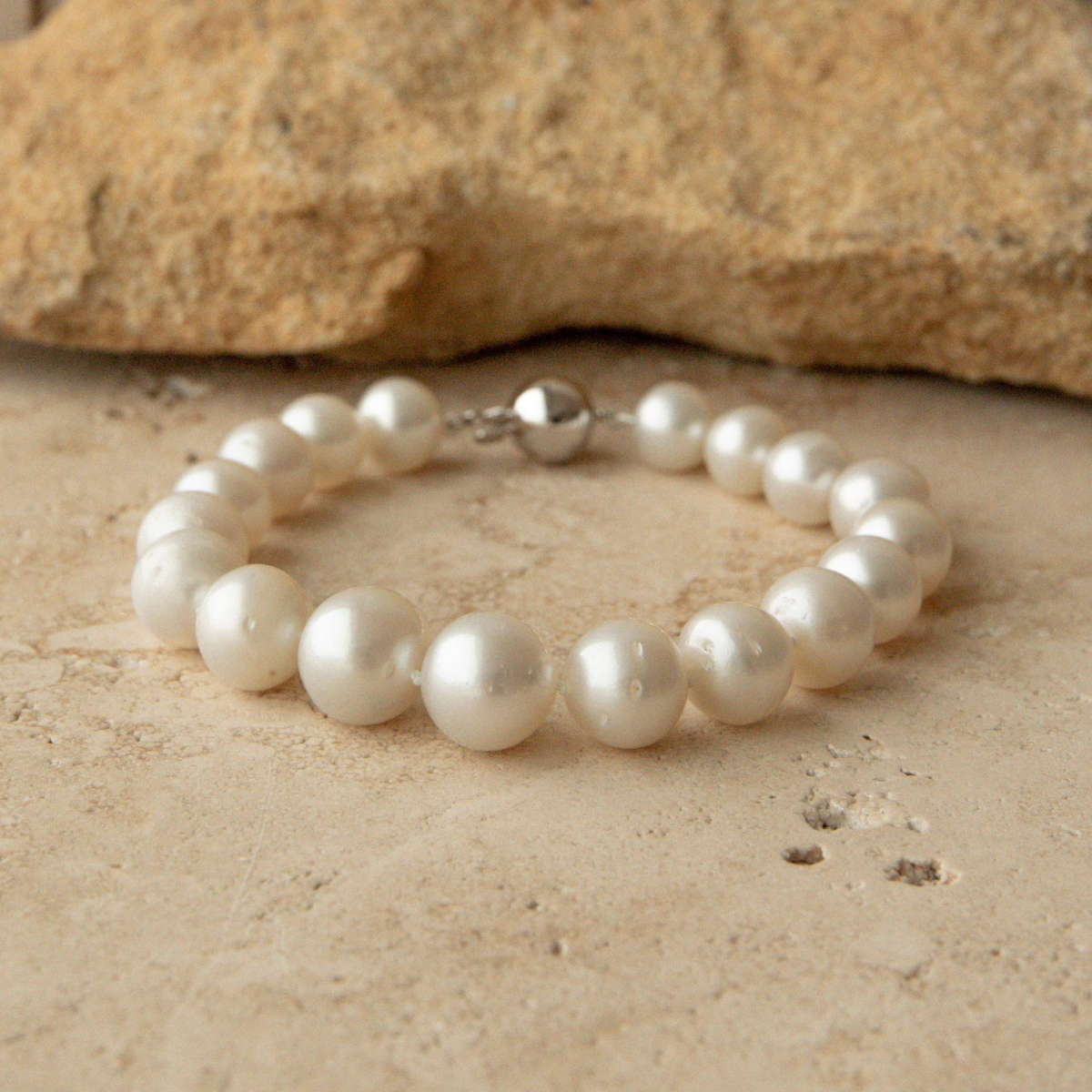 Pearl strand bracelet on a sandy surface with a rock in the background