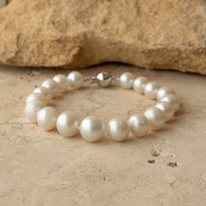 Pearl strand bracelet on a sandy surface with a rock in the background