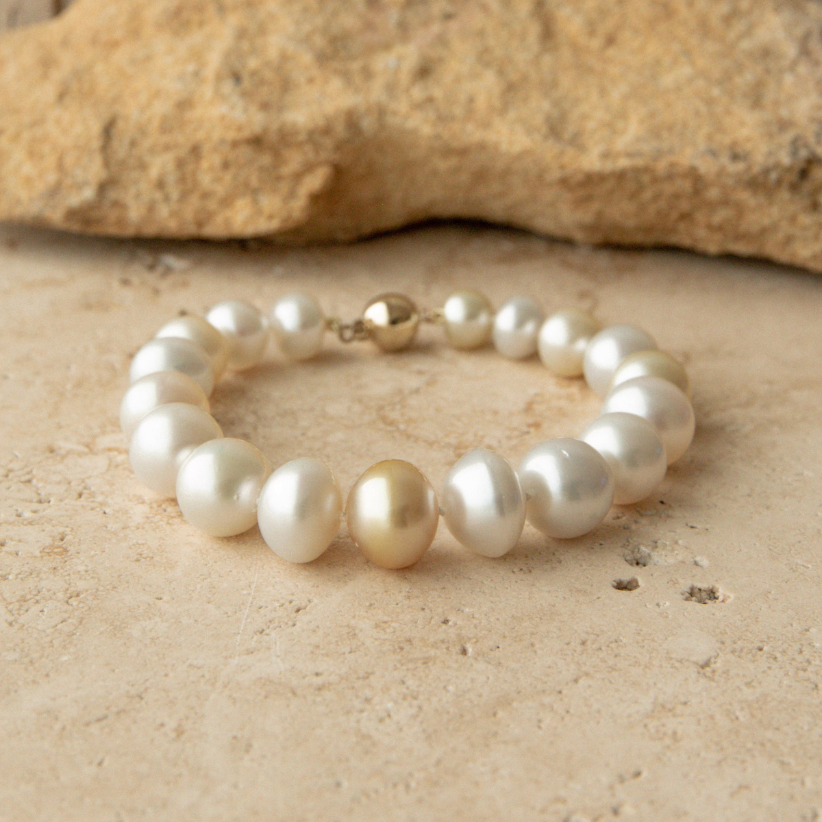 Multicolour pearl strand bracelet on a sandy surface with a rock in the background