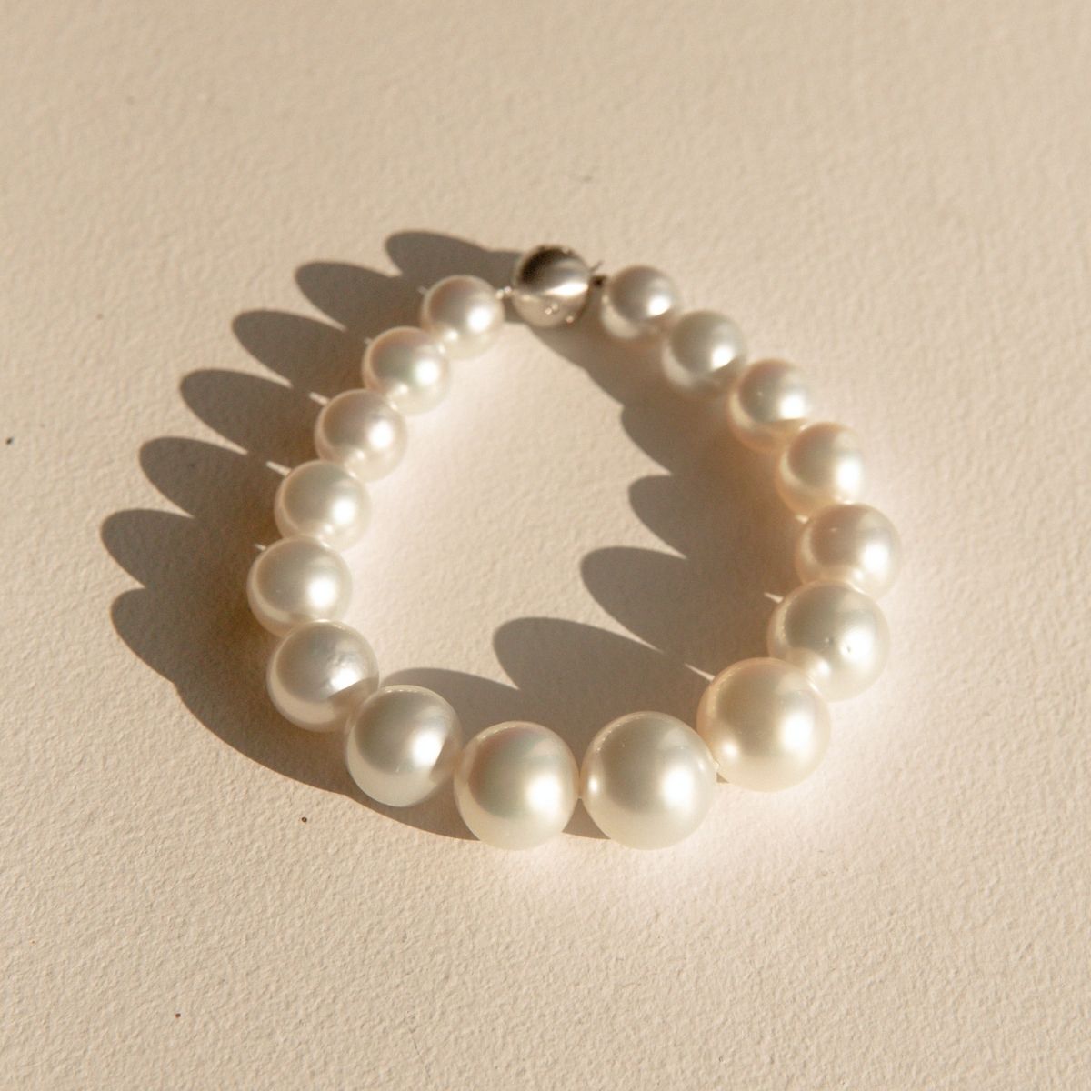 A single-strand Australian pearl bracelet with a polished 9ct white gold clasp, displayed on a textured beige surface with soft shadows.
