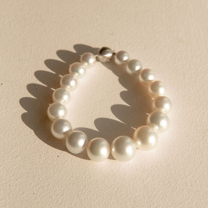 A single-strand Australian pearl bracelet with a polished 9ct white gold clasp, displayed on a textured beige surface with soft shadows.