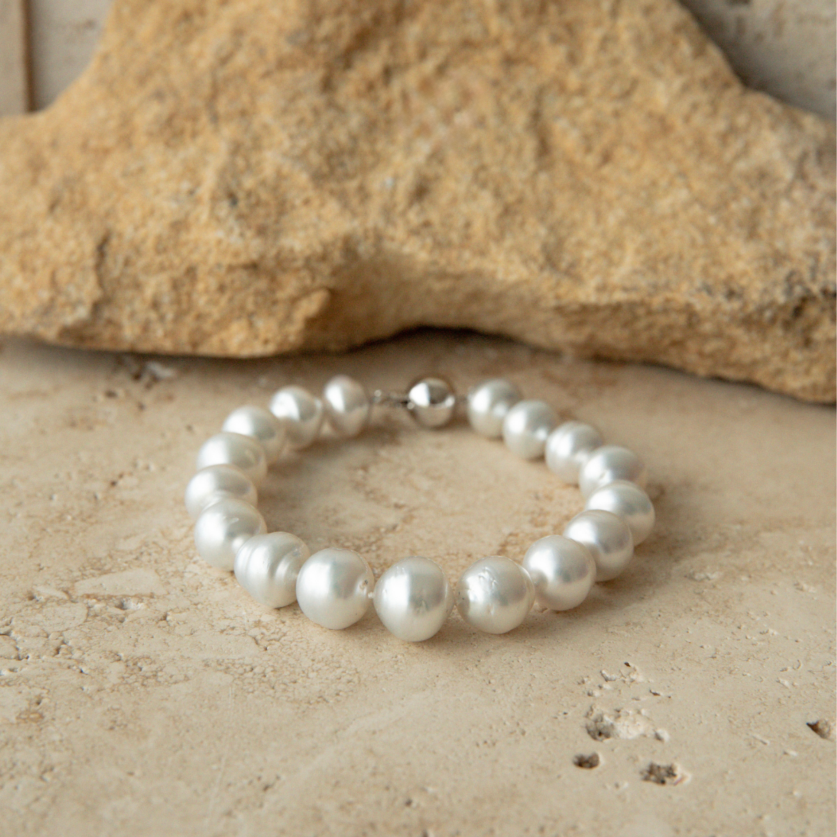 Pearl strand bracelet on a sandy surface with a rock in the background