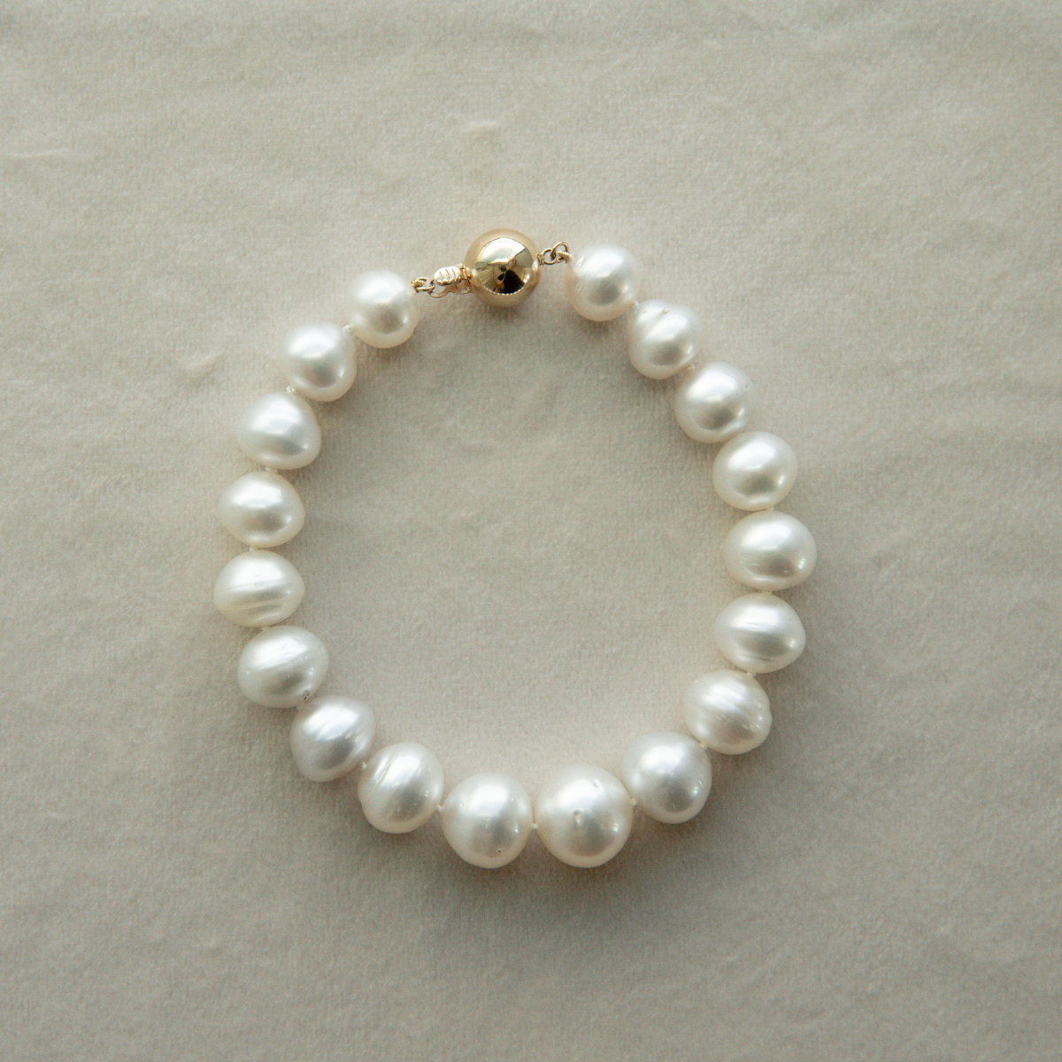 Pearl strand bracelet with a gold clasp on a light grey background