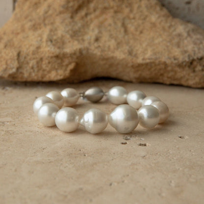 A bracelet made of large, lustrous white Australian South Sea pearls with a small 9ct white gold clasp, displayed on a textured beige stone surface with a larger rock in the background.
