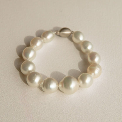 A pearl bracelet made of irregular Cygnet Bay grown Australian South Sea pearls with a polished solid gold clasp, resting on a textured light beige surface.