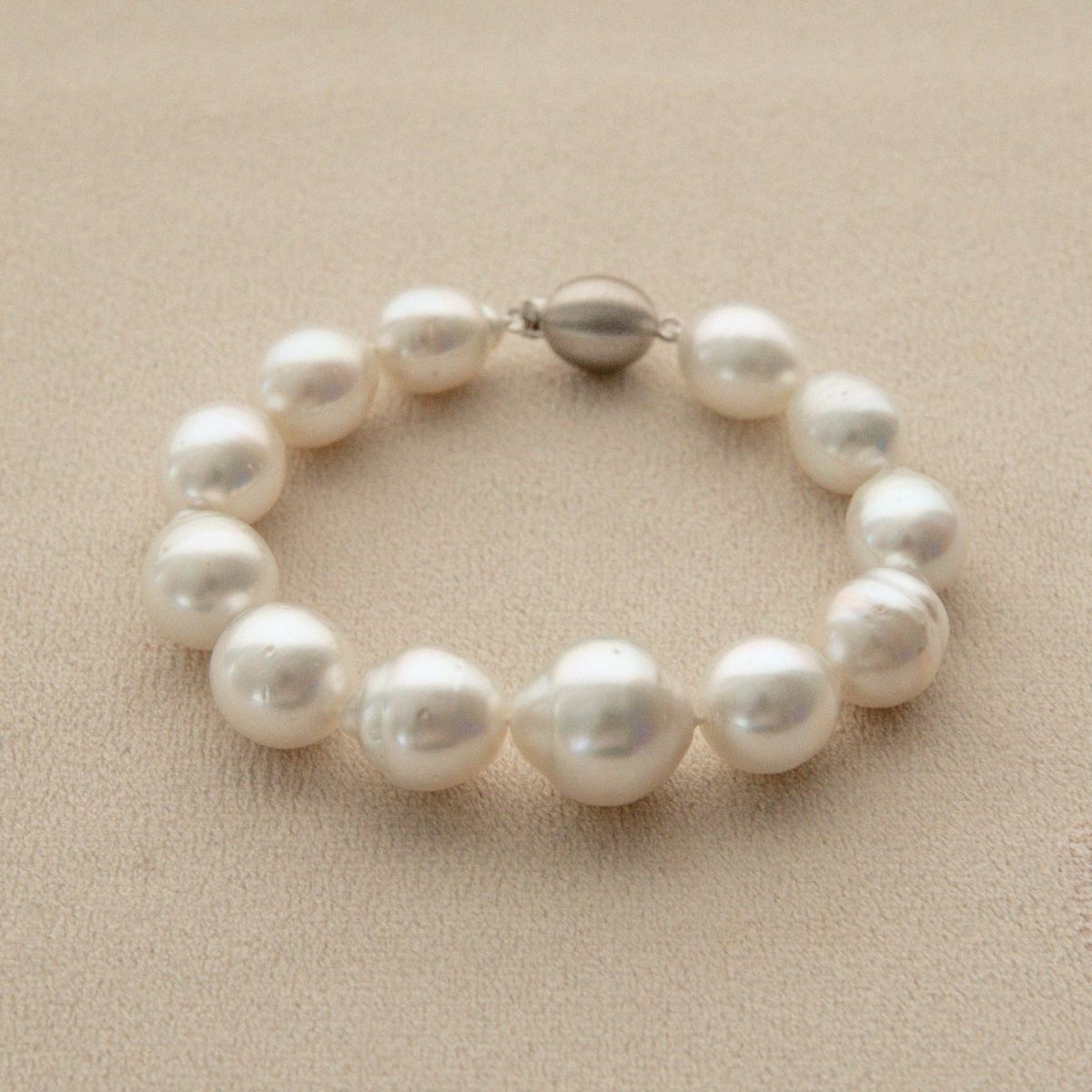 A pearl strand bracelet made of irregular white Australian South Sea pearls, featuring a small 9ct white gold clasp, displayed on a neutral beige textured background.