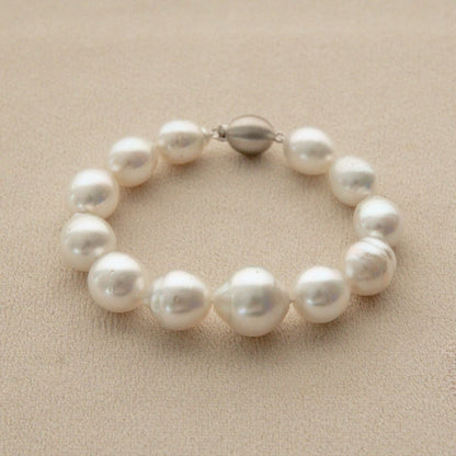 A pearl strand bracelet made of irregular white Australian South Sea pearls, featuring a small 9ct white gold clasp, displayed on a neutral beige textured background.