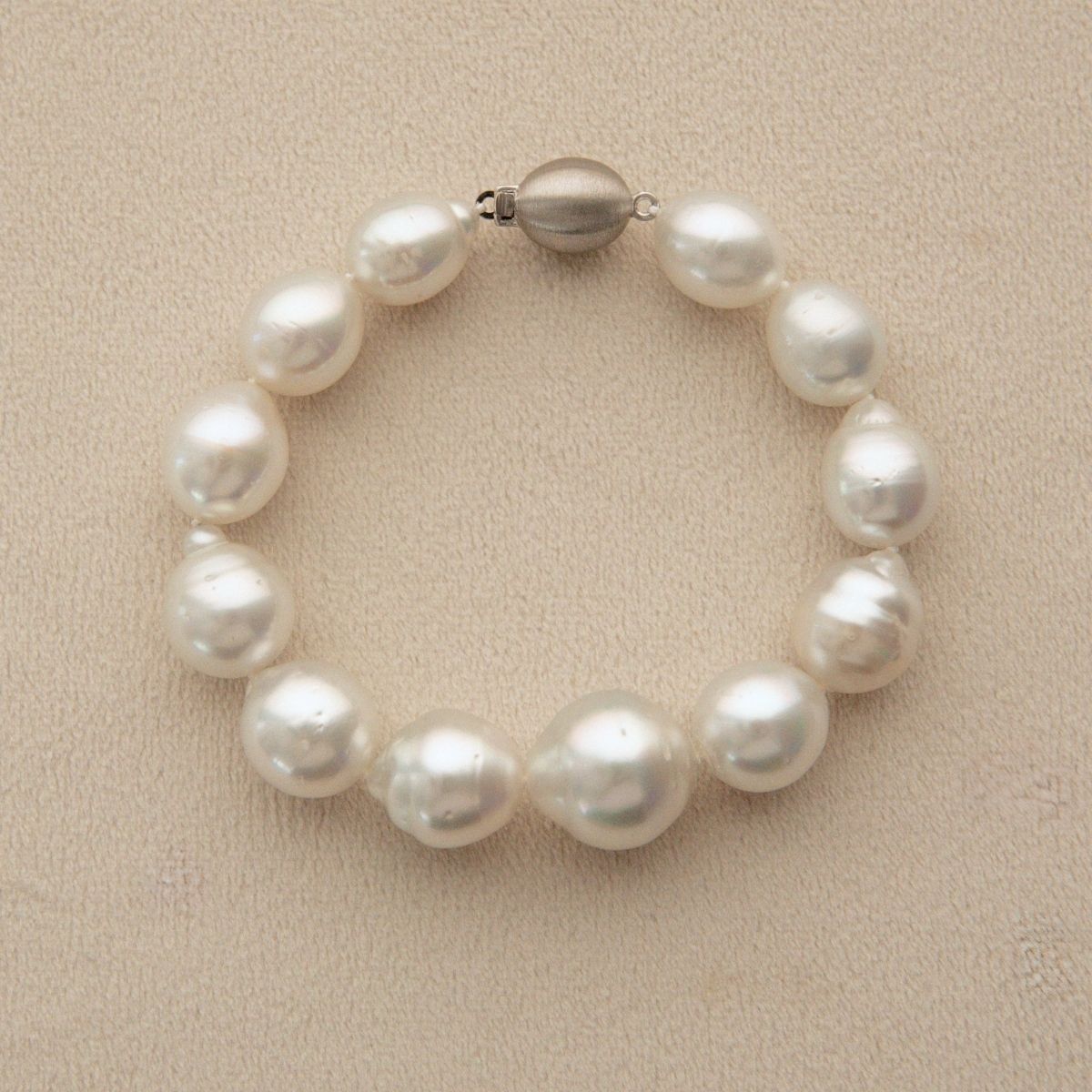 A circle shape pearl strand bracelet with a 9ct white gold metal clasp, displayed on a textured beige surface.