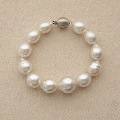 A circle shape pearl strand bracelet with a 9ct white gold metal clasp, displayed on a textured beige surface.