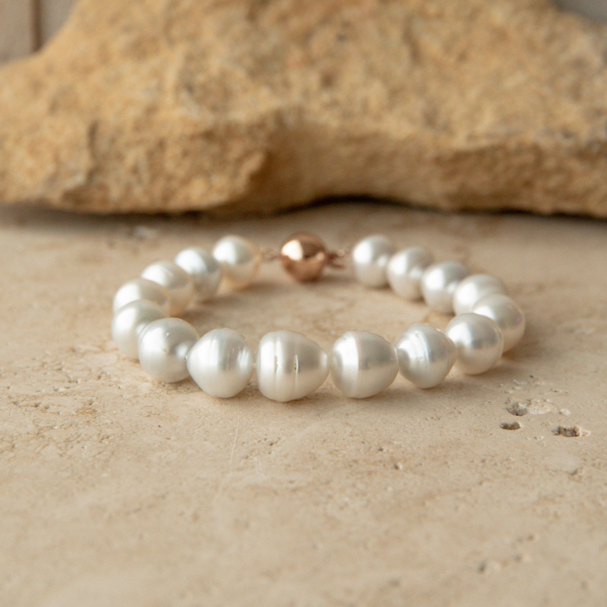 Pearl strand bracelet on a textured beige surface with a stone in the background