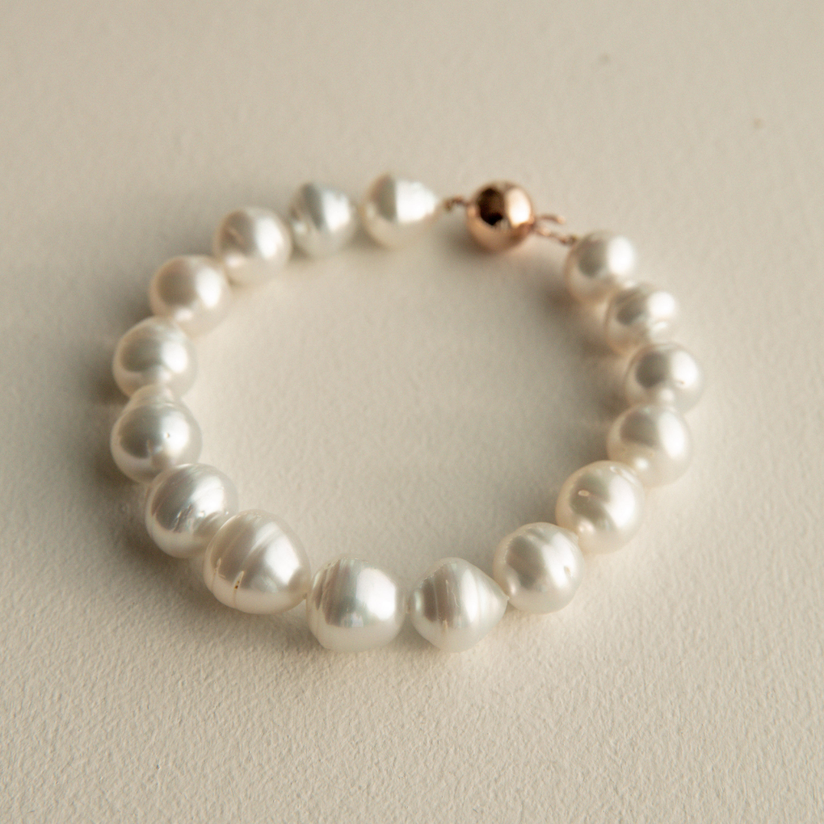Pearl strand bracelet with a rose gold clasp on a light beige background